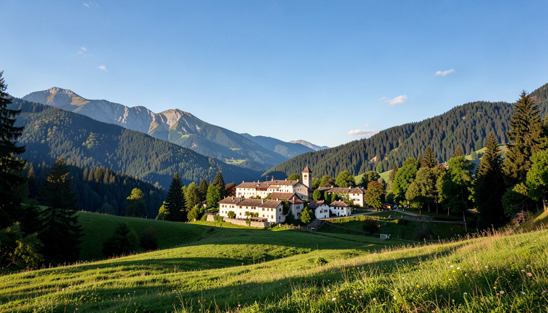 Piccolo borgo alpino con edifici bianchi e tetti in terracotta, una torre campanaria e prati verdi tra le colline